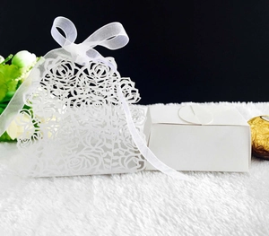 Laser-cut white wedding favor box with rose patterns and elegant ribbon bow detail