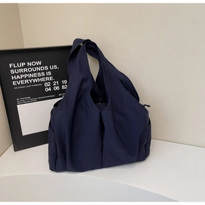 Détail d'un grand sac cabas bleu foncé avec poches latérales sur un socle blanc