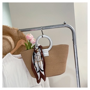 Detail of woven straw tote bag featuring silver ring handles and stylish printed scarf