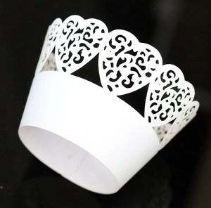 Detailed laser-cut white cupcake wrapper with heart patterns and crown edge on black background