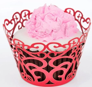 Close-up of laser-cut red paper cupcake wrapper with intricate hollow heart and vine patterns