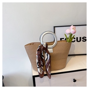 Detail of woven straw tote bag with silver metal handles and decorative printed silk scarf