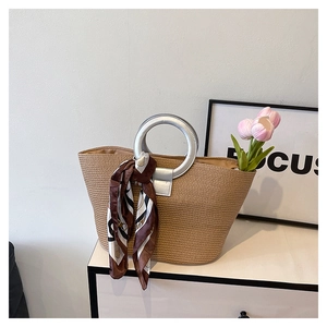 Detail of woven straw tote bag with silver metal ring handle and floral silk scarf