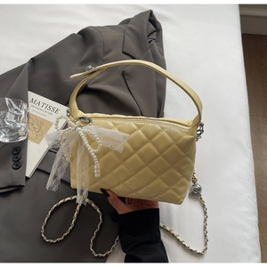 Detail of yellow quilted bag with pearl bow pendant and silver chain strap details