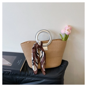 Detail of straw woven tote bag featuring silver round handles and decorative floral scarf