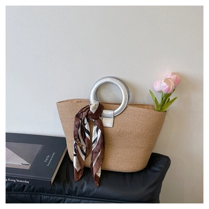 Detail of woven straw tote bag with silver circular metal handle and decorative silk scarf