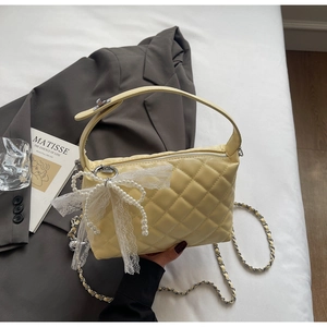 Close-up of yellow quilted chain bag with pearl lace bow charm on bed setting