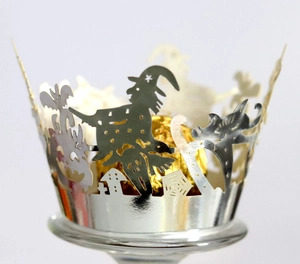 Laser-cut silver Halloween cupcake wrapper with witch and castle patterns on glass base