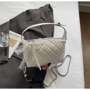 Detail of white quilted handbag with pearl bow and lace charm on a soft background