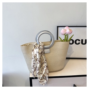 Detail of woven straw tote bag with round silver handle and decorative printed silk scarf