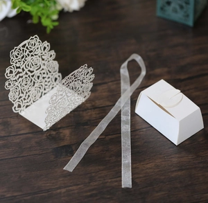 Macro detail of laser-cut rose patterns on white wedding candy box with silk ribbon