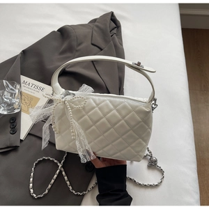 Detail of white quilted handbag featuring lace bow, pearl charm and silver chain strap