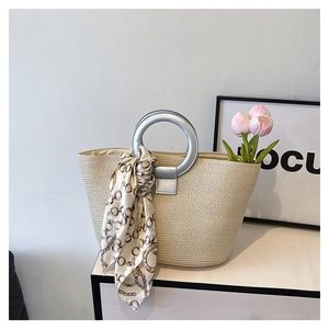 Close-up of woven straw tote bag with silver metal handle and decorative chain scarf