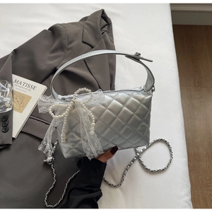 Detail of silver quilted texture with lace bow and pearl chain on stylish handbag