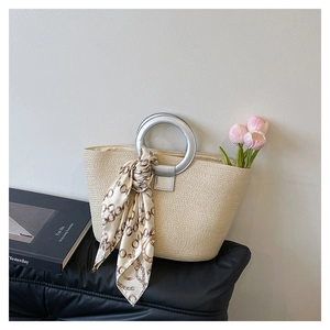Detail of woven straw tote bag with silver ring handle and decorative silk scarf