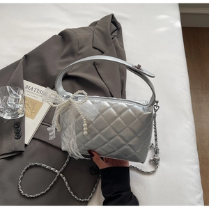 Close-up of silver quilted handbag with lace bow, pearl charms and metal chain strap