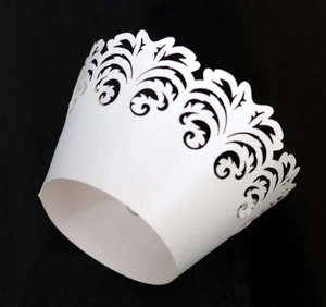 Macro detail of white laser-cut cupcake wrappers with intricate floral vine lace patterns