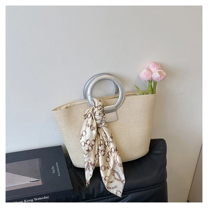 Detailed close-up of woven beige tote bag with silver ring handles and silk scarf detail