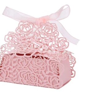Detail of pink laser-cut wedding favor box featuring intricate rose patterns and a silk ribbon