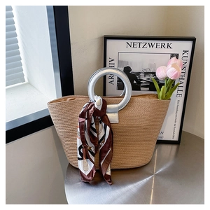 Detail of woven straw tote bag featuring round metallic handles and a decorative silk scarf