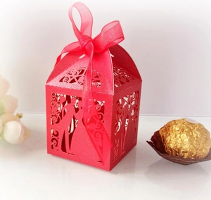 Macro detail of red laser-cut wedding favor box with ribbon and bride groom patterns