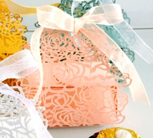 Detail of laser-cut rose hollow favor boxes with organza ribbons in multiple colors