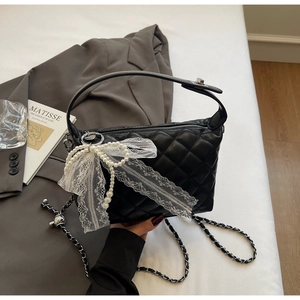 Close-up of black quilted bag with lace bow, pearl tassels and woven chain strap