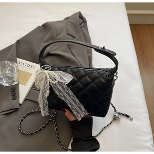 Detail of black quilted leather handbag with white lace bow and elegant pearl charm