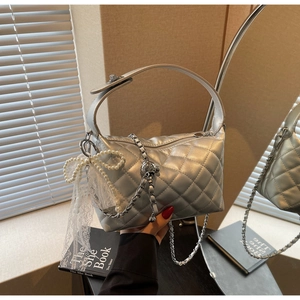 Close-up of silver quilted handbag featuring pearl bow charms and elegant metal chain strap
