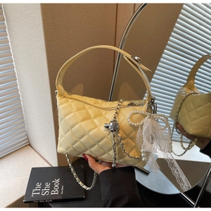 Detail view of yellow quilted handbag featuring pearl lace bow and metal ball charm