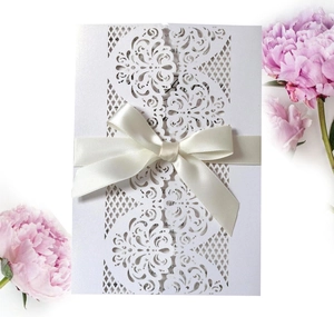 Detailed laser-cut pattern on white wedding invitation with cream satin ribbon bow