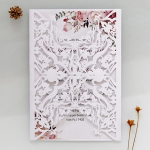 Detailed laser-cut white wedding invitation featuring intricate floral hollow patterns and inner card