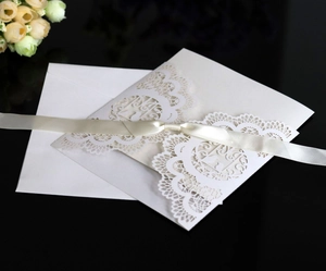 Detail of white laser-cut lace wedding invitation with a silk ribbon bow and envelope