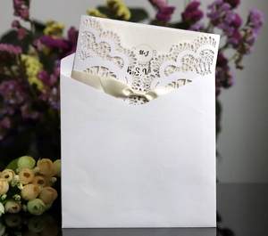 Laser cut wedding invitation with cream silk bow and white envelope on mirror surface