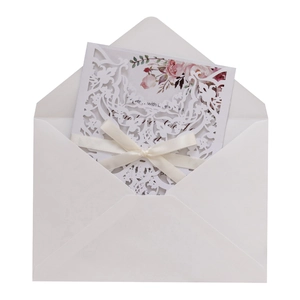 Detail of laser-cut white wedding invitation with floral insert and cream silk bow