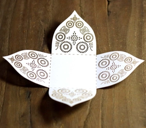 Detailed view of laser-cut white wedding favor box in flat-spread layout on wood