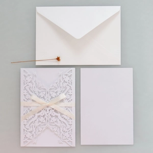 Macro detail of laser-cut floral wedding invitation with cream satin ribbon and envelope