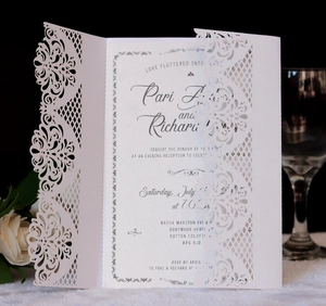Detail of laser-cut wedding invitation with white intricate lace pattern on black surface