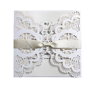 Macro detail of laser cut wedding invitation with white lace pattern and satin ribbon