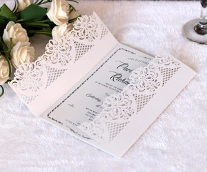 Close-up of white laser-cut lace invitation with elegant blue floral inner card