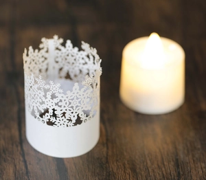 Close-up of white paper candle shade with laser-cut snowflake patterns on wood