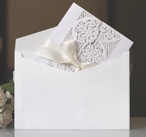 Macro detail of laser cut floral wedding invitation with cream silk ribbon bow and envelope