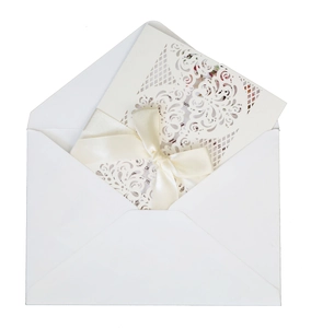 Detail of laser-cut wedding invitation featuring a cream silk bow and elegant floral patterns