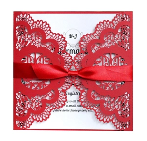 Detail of red laser-cut wedding invitation with satin bow and white inner card