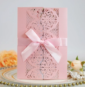 Detail showing pink laser-cut floral wedding invitation with silk bow on a porcelain plate