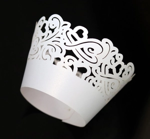 Detailed laser-cut white cupcake wrapper with heart lace pattern on a black background