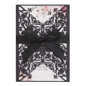 Detail of laser cut wedding invitation with black hollow pattern and satin ribbon bow