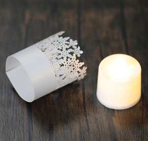 Macro view of white snowflake laser-cut paper candle sleeves on dark wood table