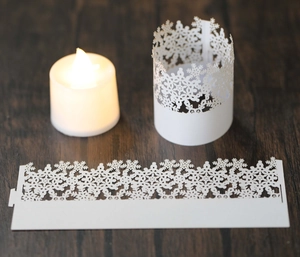Detail of white laser-cut snowflake paper candle covers on a rustic wooden table