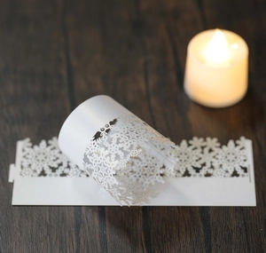Close-up of white laser-cut snowflake paper candle wraps on dark wood surface